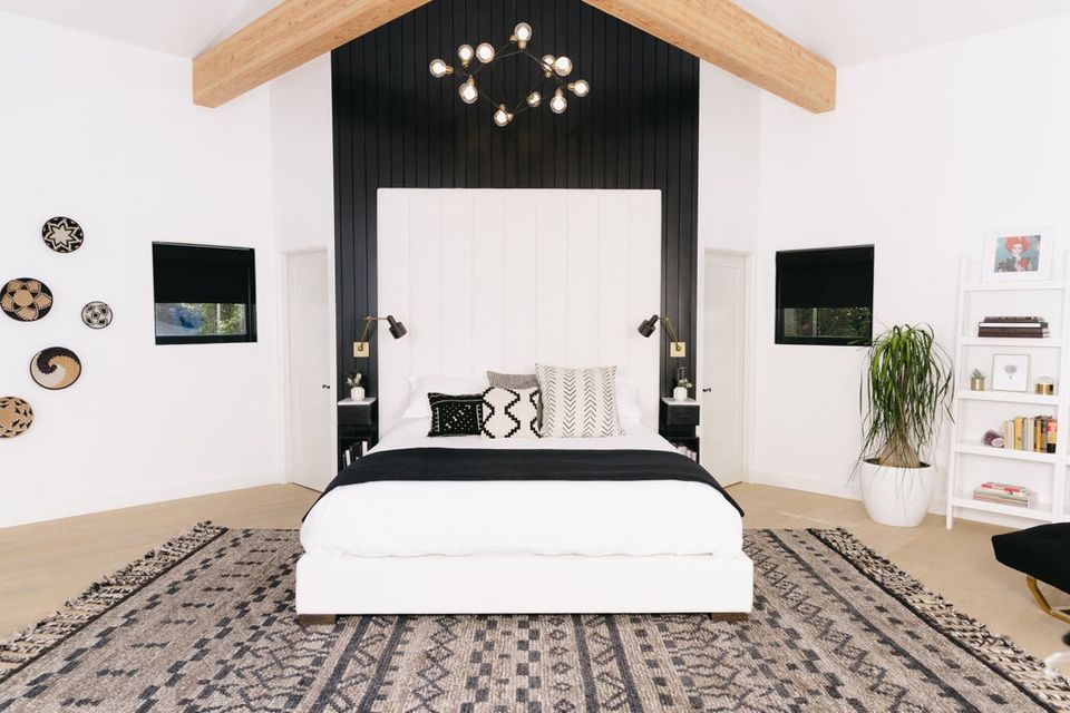 Modern bedroom with black accent wall, white bedding, geometric patterned rug, and minimalist Scandinavian decor