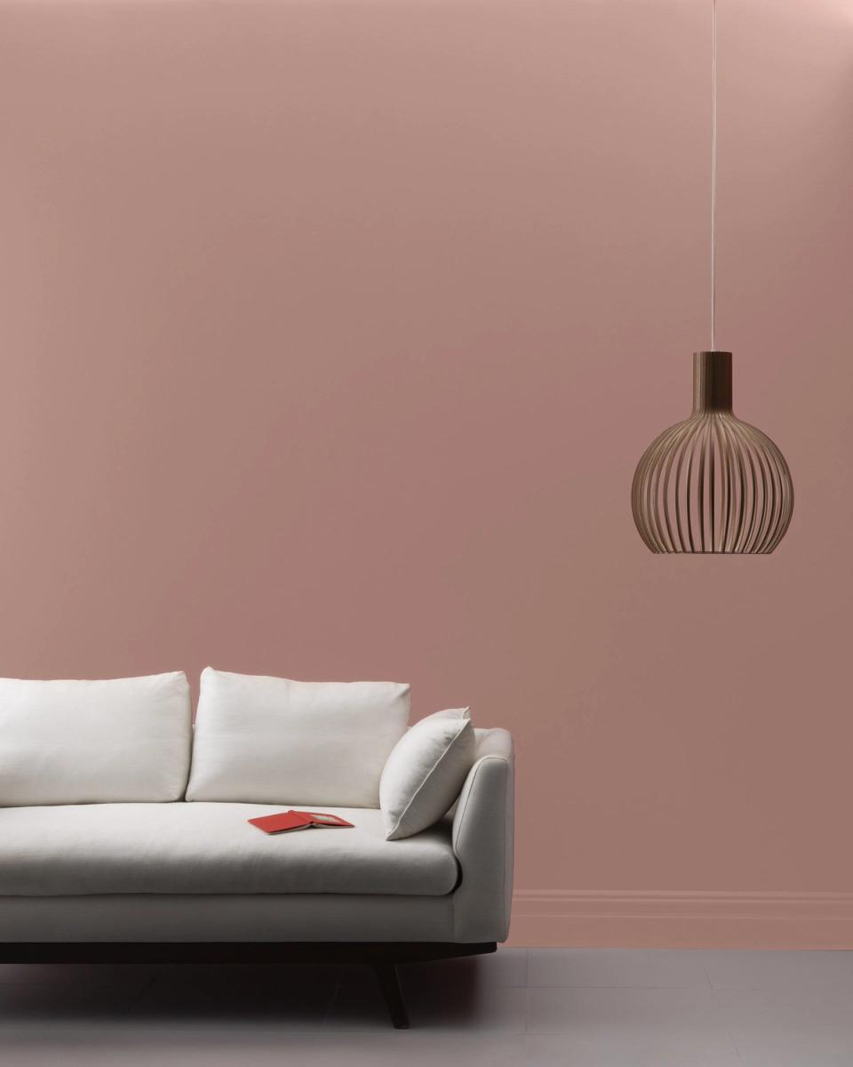 Minimalist mauve living room with cream sofa, sculptural pendant light, and expansive empty wall evoking calm, contemporary elegance.