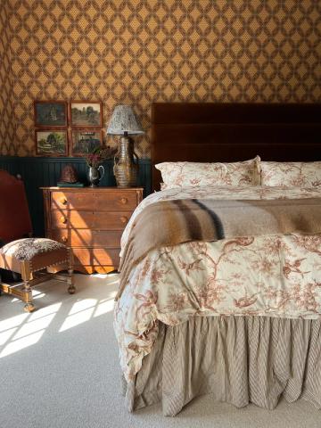 Vintage-inspired bedroom with warm damask accent wall, floral bedding, and antique wood furnishings