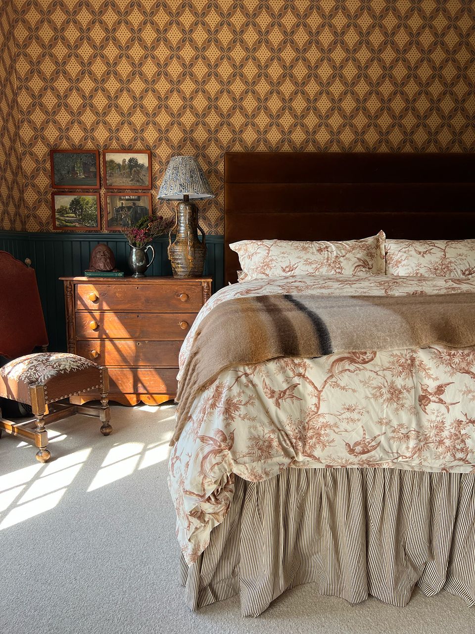 Vintage-inspired bedroom with warm damask accent wall, floral bedding, and antique wood furnishings