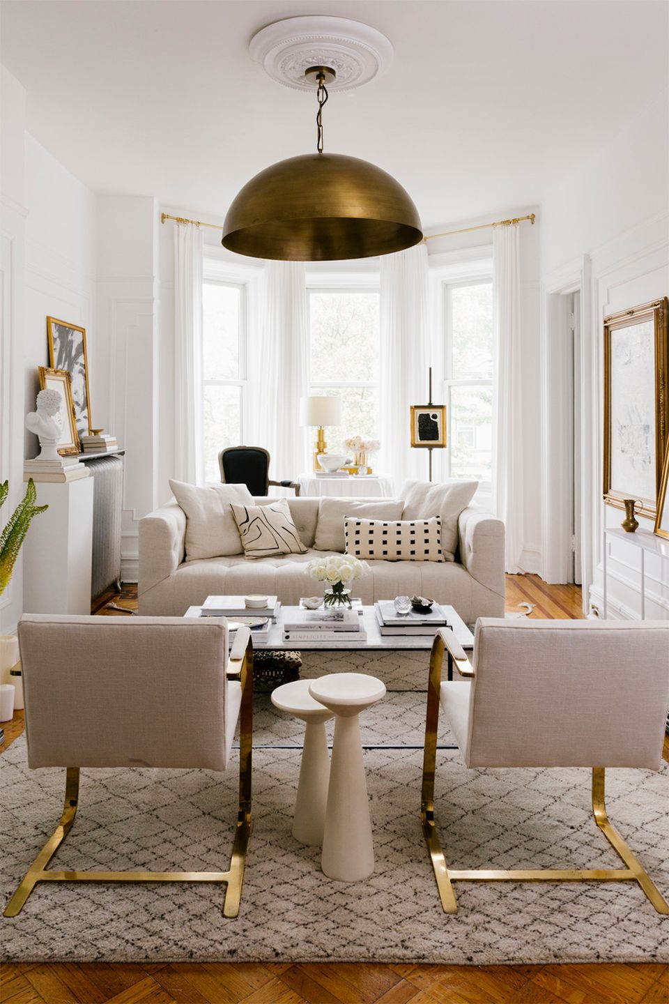 Modern living room with warm brass dome pendant, neutral upholstery, gold-accented furniture, and bright natural light