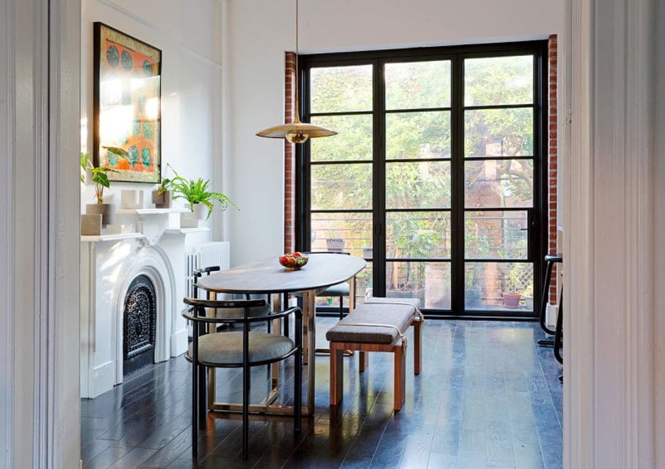 Bright scandinavian dining space with black table, fireplace, and garden views through glass doors