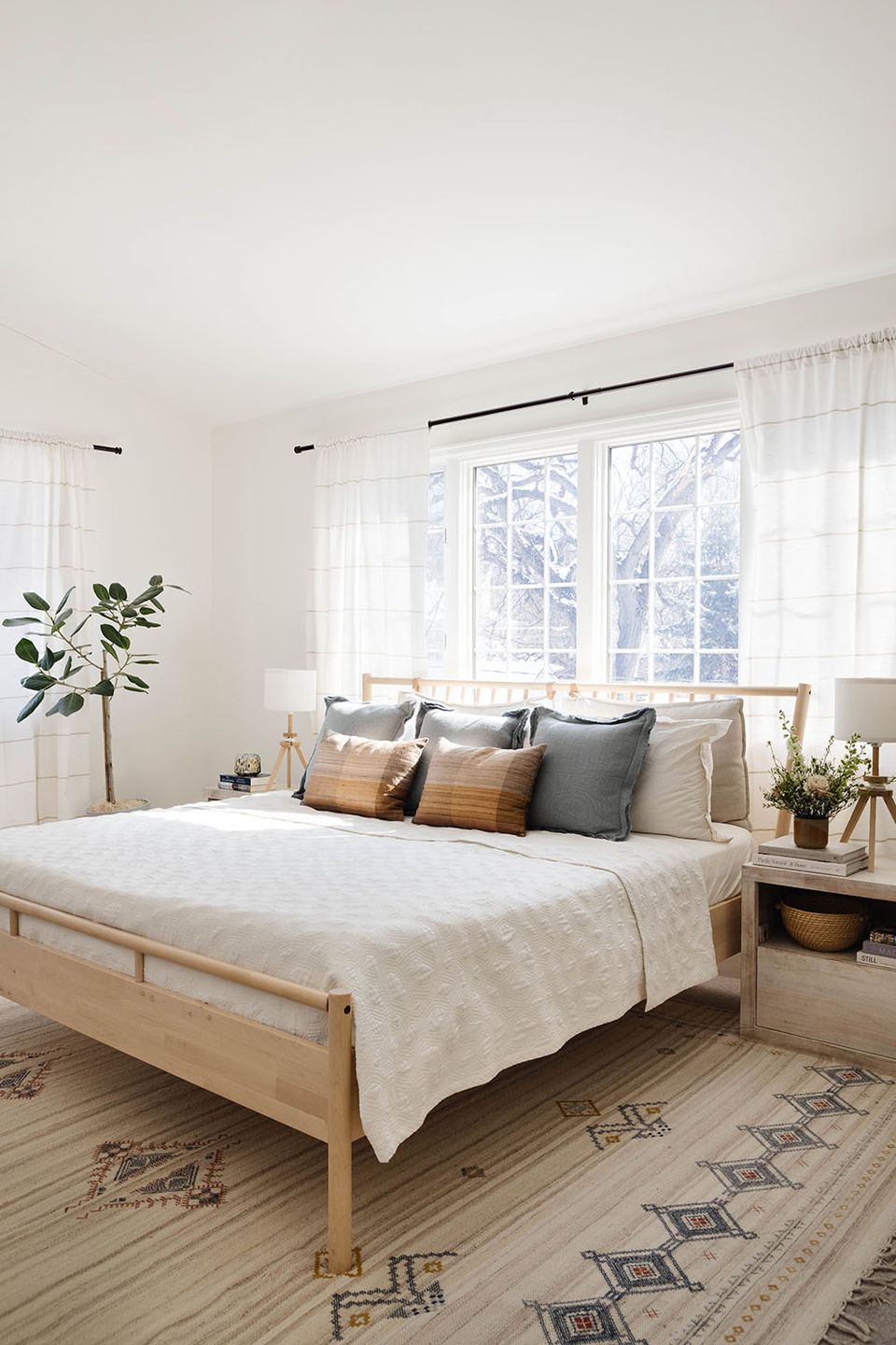 Serene bedroom with light wood platform bed, neutral tones, layered textures, and plants.