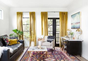 Transitional living room with gold curtains, dark sofa, jewel-toned rug, and botanical accents