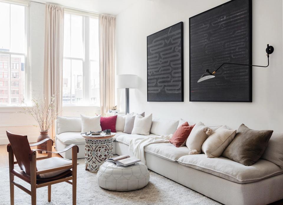 Contemporary living room with black wall art panels, cream sectional, jewel-tone accents, and soft natural light from tall windows
