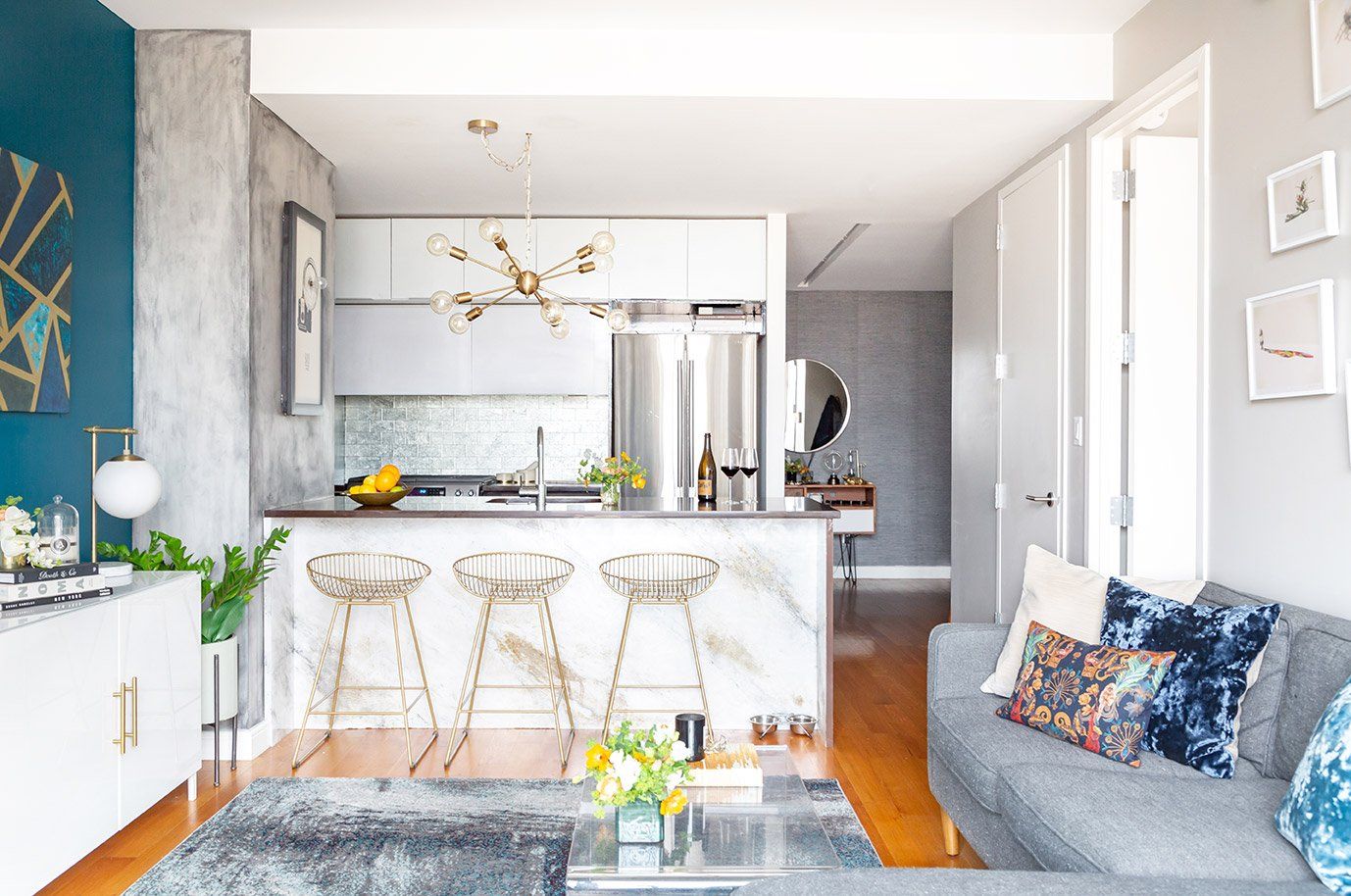 Bright open-concept kitchen and living room with teal accent wall, white cabinetry, and natural wood flooring creating an airy, modern space