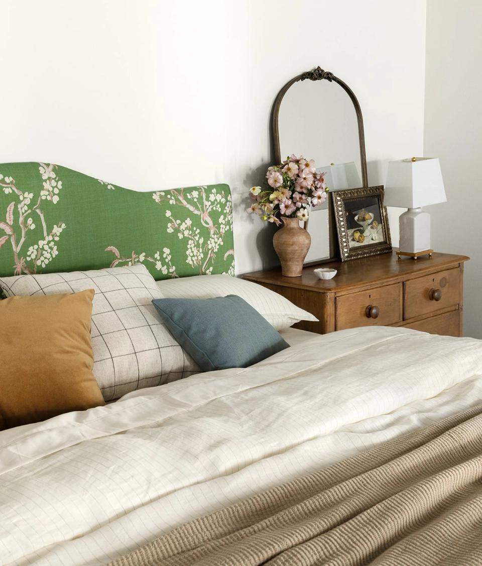 Eclectic bedroom blending earthy tones with green floral headboard, mustard and slate blue pillows, and vintage wood furniture