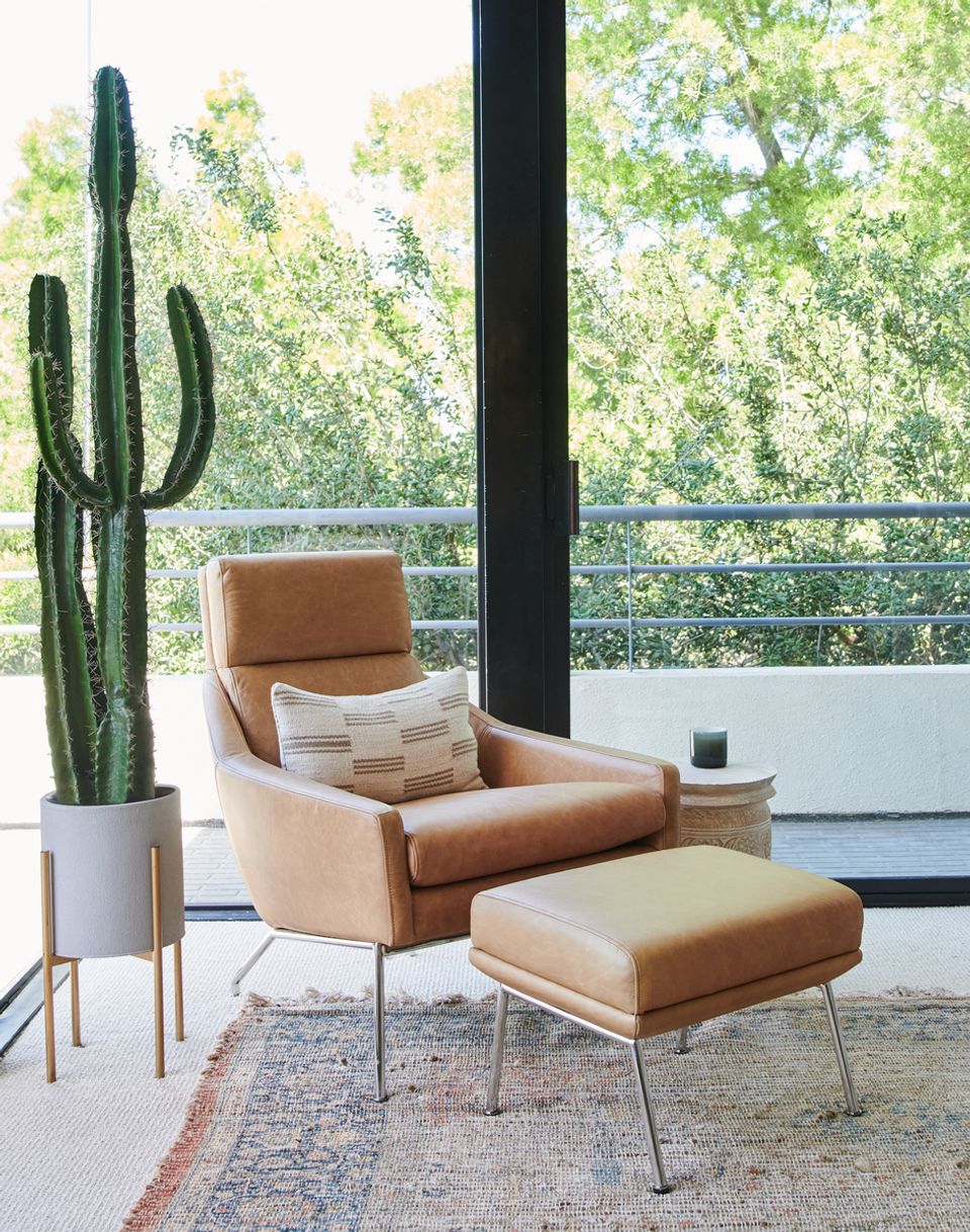 Warm mid-century lounge corner with cognac leather chair, potted cactus, and panoramic nature views