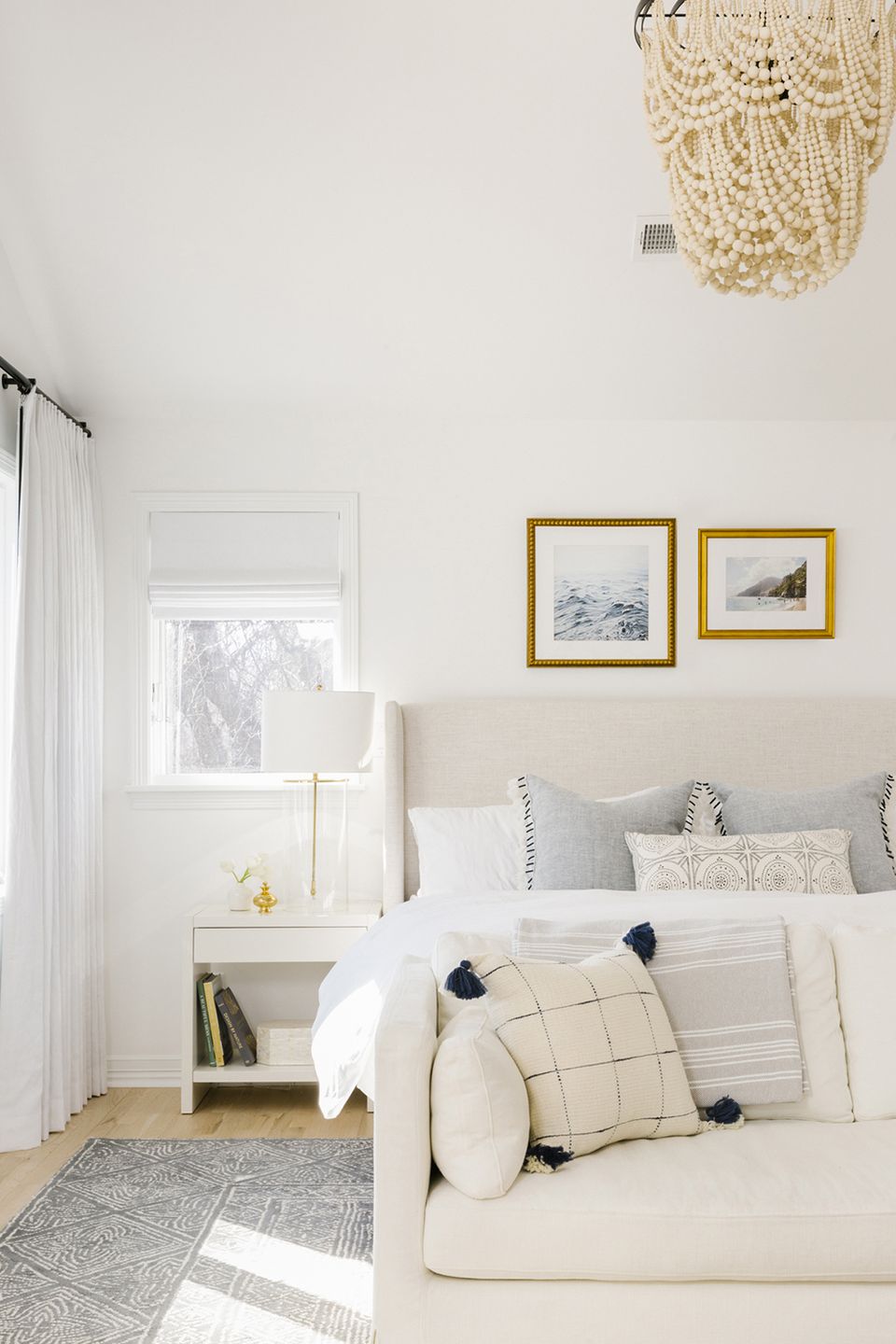 Scandinavian-inspired bedroom with cream upholstered bed, gold-framed art, and natural woven pendant light