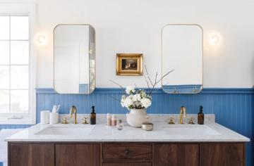 Spa-inspired bathroom with blue shiplap wainscoting, dual vanity with dark wood cabinetry, and soft brass sconces creating a serene coastal aesthetic.