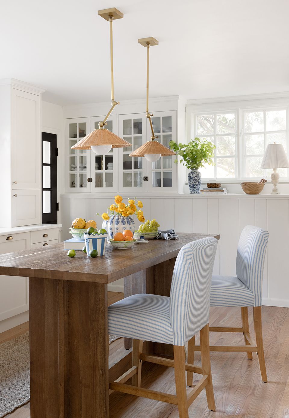Scandinavian-inspired dining space combining crisp white kitchen with warm wood table, natural wood pendant lights, and soft striped seating