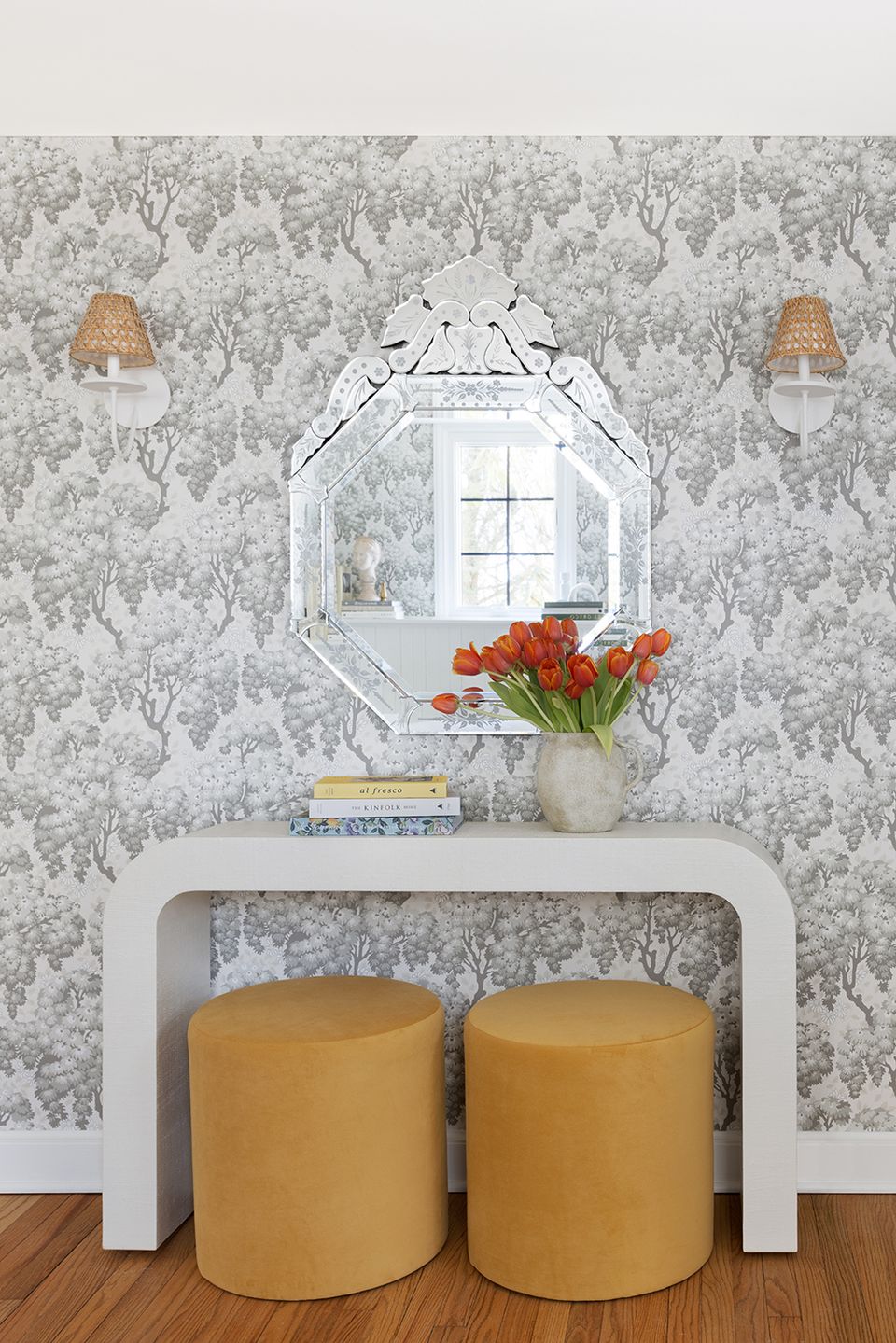 Elegant entryway features floral wallpaper, curved white console table, and mustard poufs creating classic cottage charm