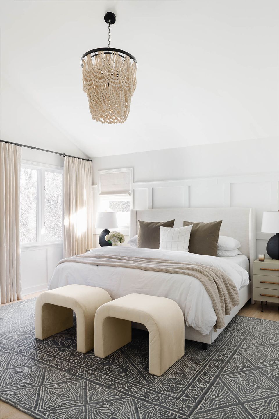 Sophisticated neutral bedroom with white paneled headboard, beaded pendant light, and cream benches