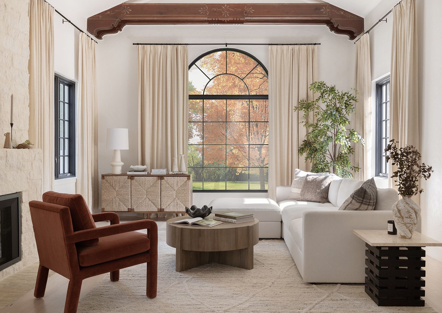 Sophisticated living room with warm wood beams, cream drapery, burgundy leather chair, and modern furnishings creating elevated, timeless elegance.