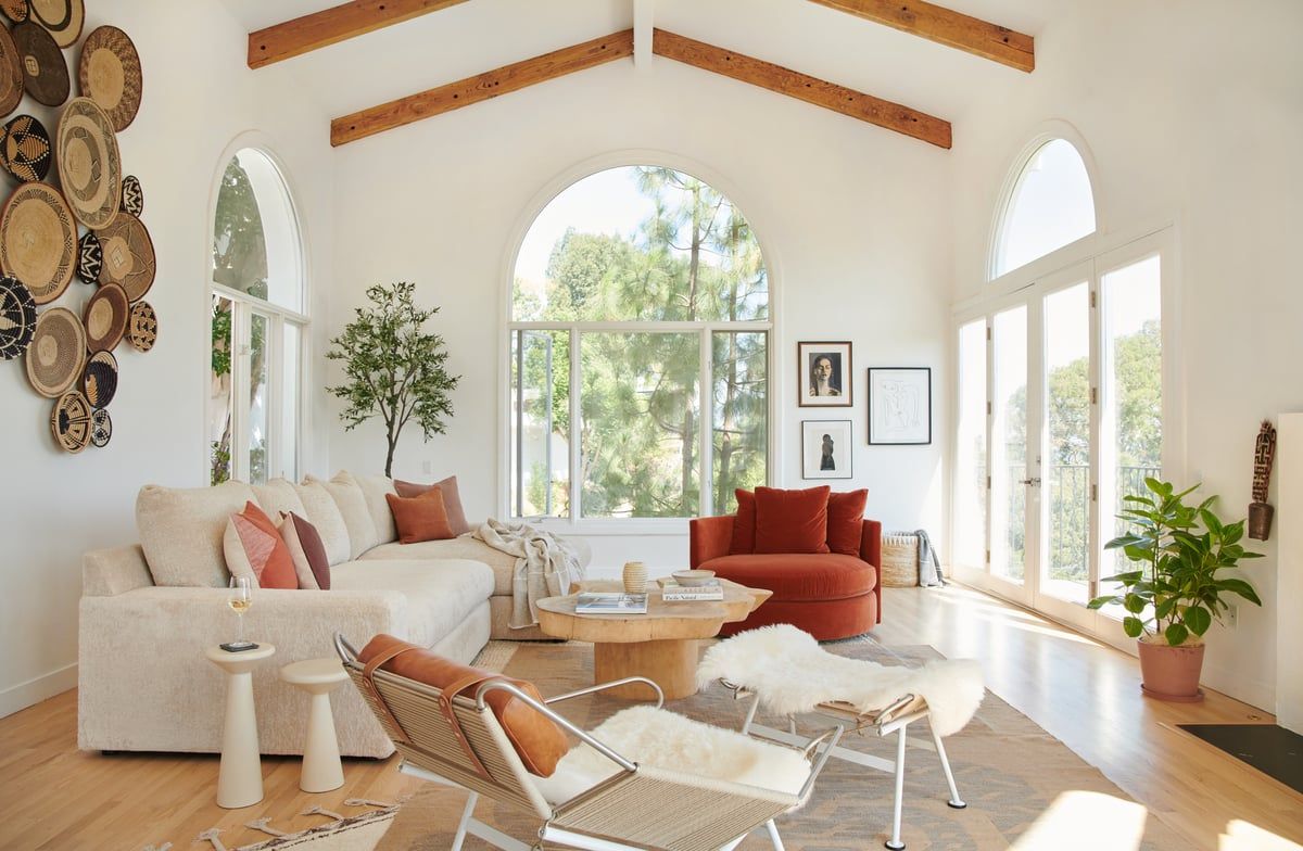 Bright living room with vaulted ceilings, warm earth tones, natural wood beams, and layered textures creating a cozy, modern rustic aesthetic.