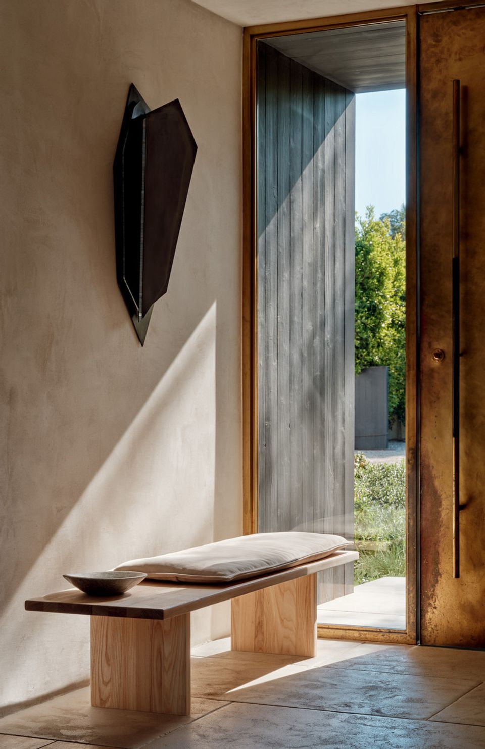 Minimalist entryway with natural wood door frame, soft plaster walls, and sculptural wall art