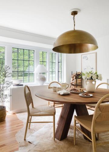 Airy dining space with brass dome pendant, wood table, rattan chairs, and soft natural light.