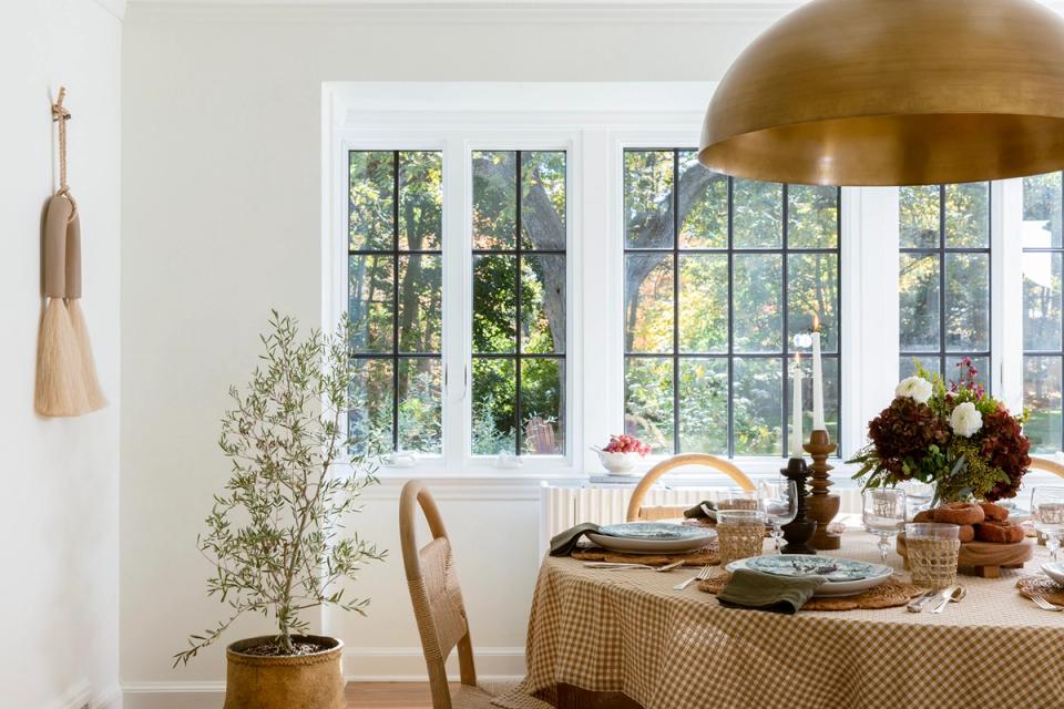 Minimalist dining space with warm brass pendant, natural wood table, and neutral palette accented by potted greenery