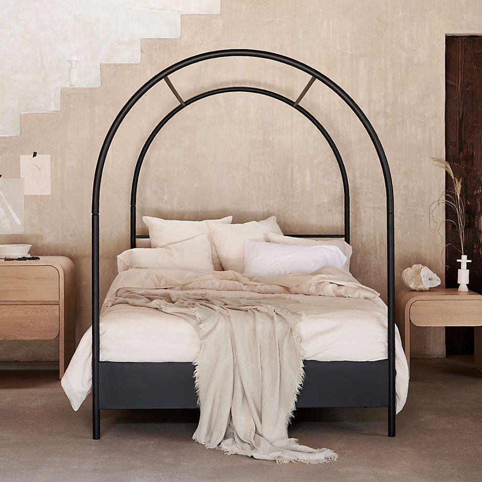 Modern minimalist arch canopy bed with black metal frame and warm neutral palette