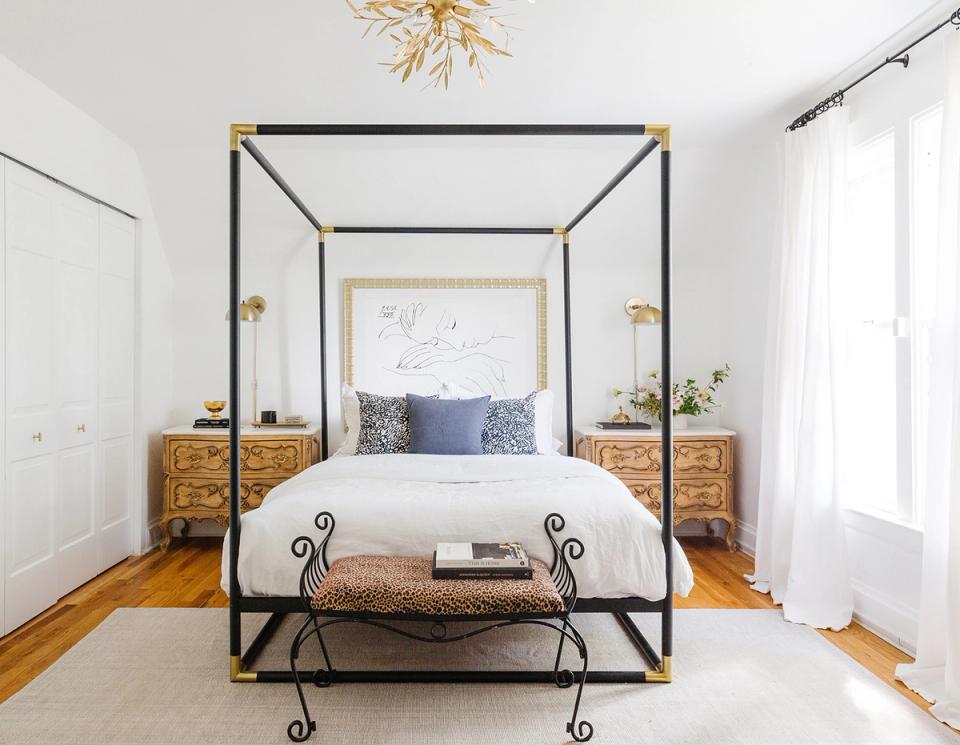 Bright modern bedroom with black canopy bed, natural wood nightstands, and minimalist white bedding