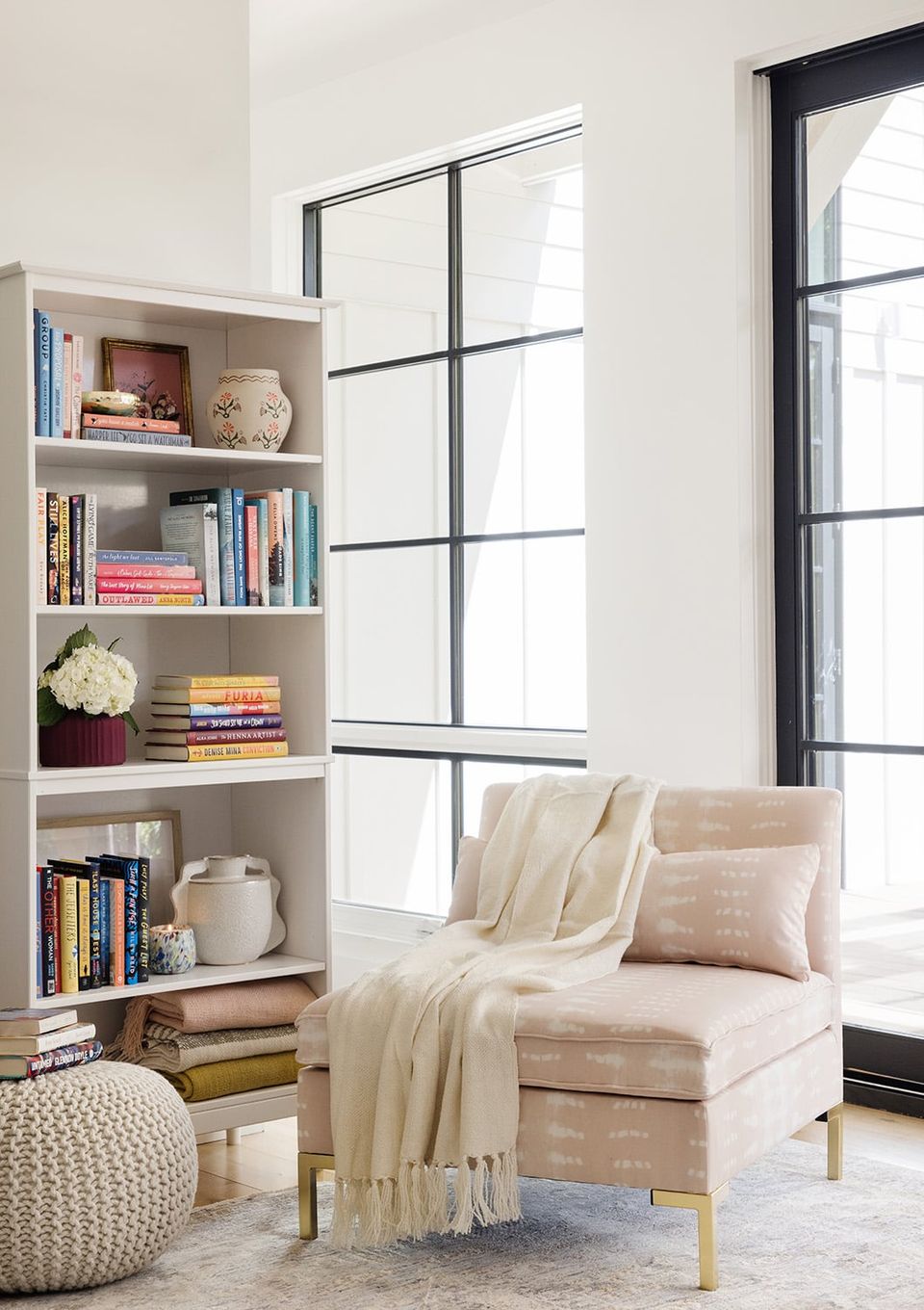 Minimalist reading corner with cream built-in shelving, soft pink armchair, and black-framed glass doors creating a serene, light-filled retreat