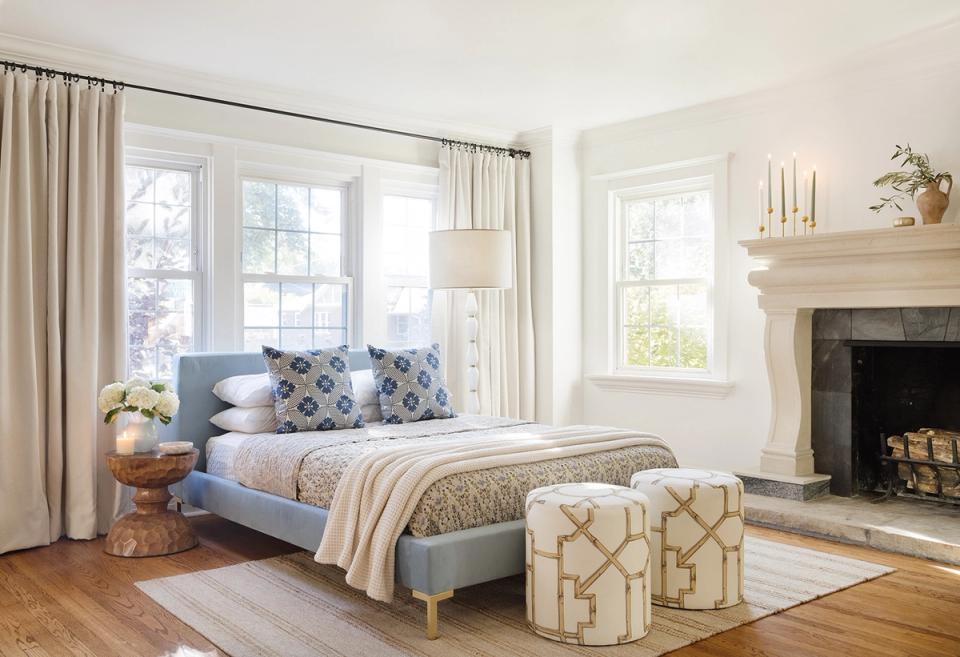 Serene bedroom with blue upholstered bed, cream curtains, fireplace, and warm wood flooring