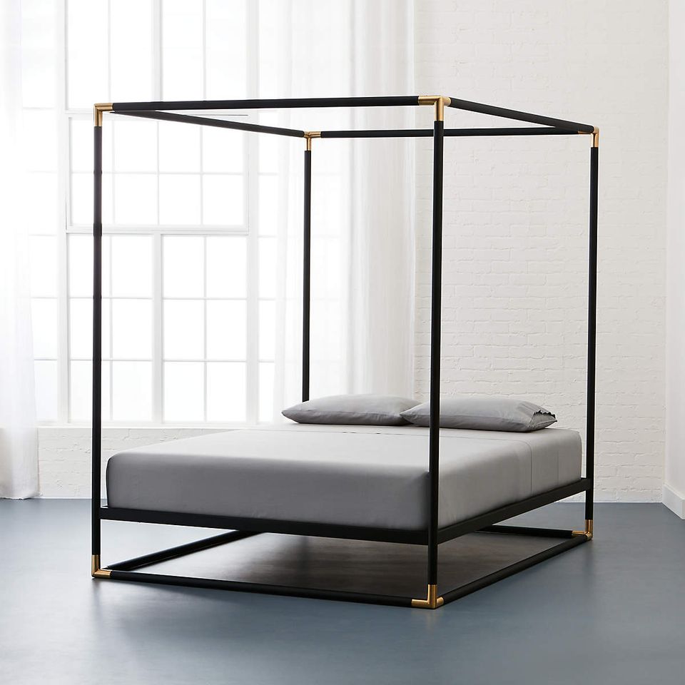 Industrial-style canopy bed with black metal frame and brass base accents