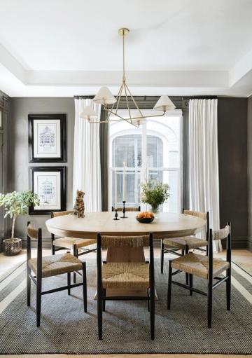 Sophisticated dining room with round wood table, charcoal walls, brass lighting, and natural textures