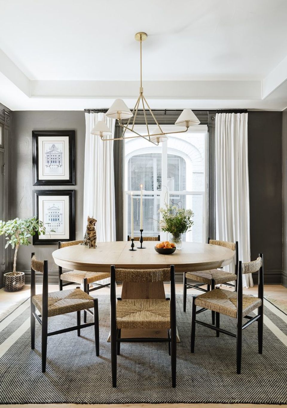 Sophisticated dining room with round wood table, charcoal walls, brass lighting, and natural textures