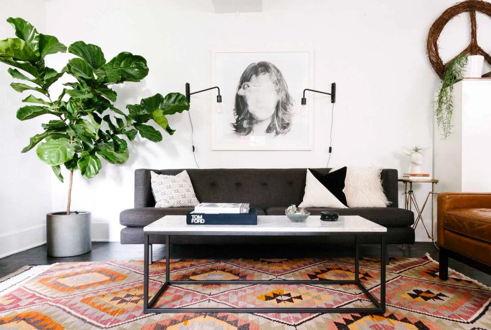 Modern eclectic living room with charcoal sofa, geometric patterned rug, lush green plants, and monochrome wall art.