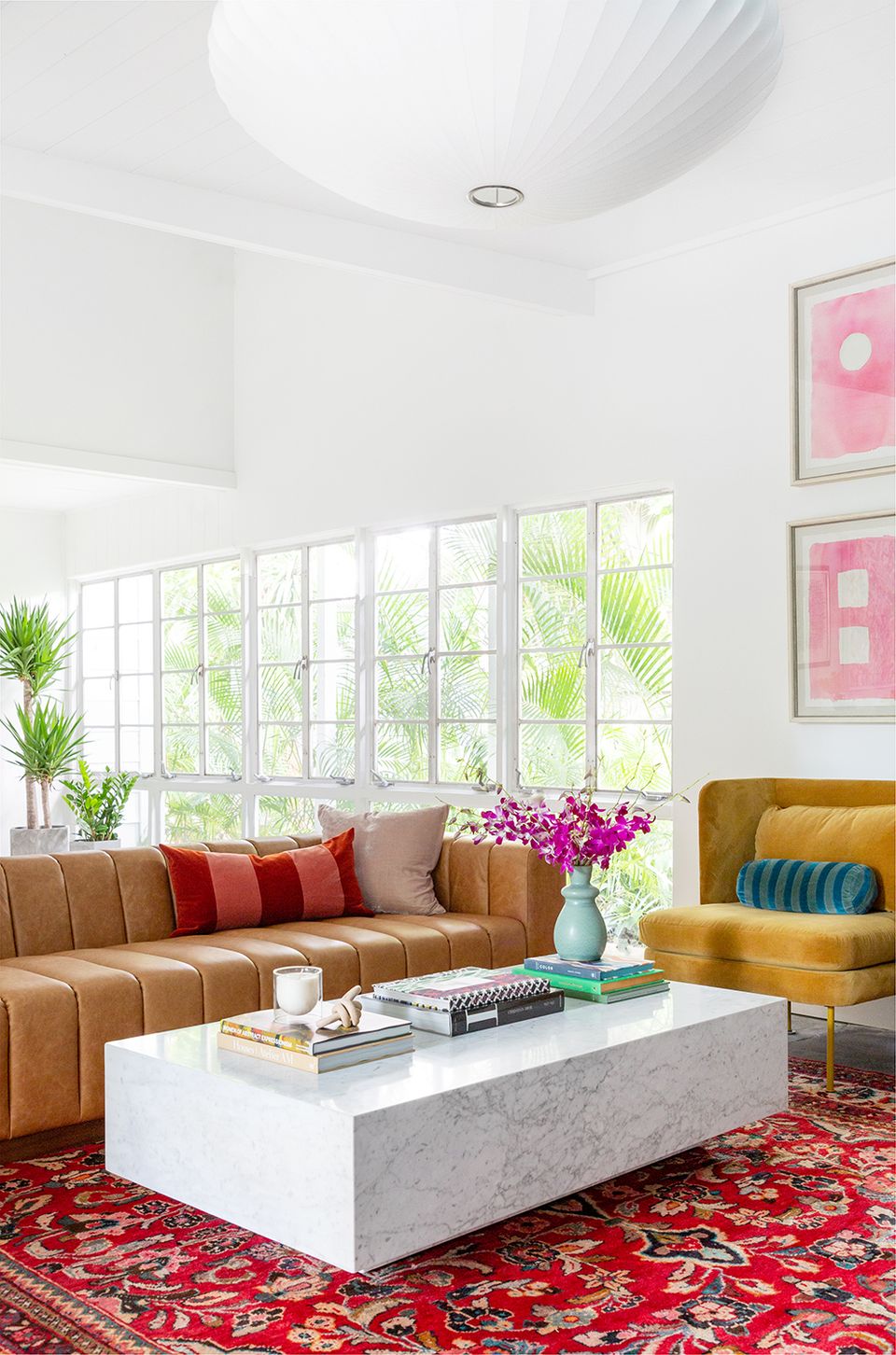 Sunlit contemporary space featuring caramel leather sectional, vibrant red patterned rug, and colorful accent pillows showcasing eclectic print mixing