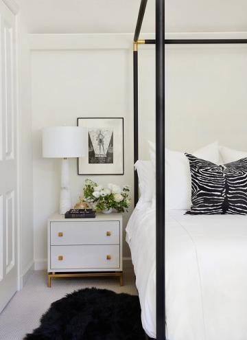Modern minimalist bedroom with black canopy bed, zebra-striped pillows, and mid-century nightstand