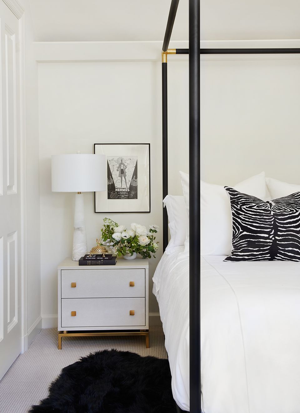 Modern minimalist bedroom with black canopy bed, zebra-striped pillows, and mid-century nightstand