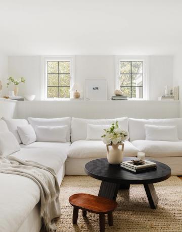 Serene minimalist bedroom lounge with crisp white bedding, black modern side table, wooden stool, and peaceful monochromatic calm