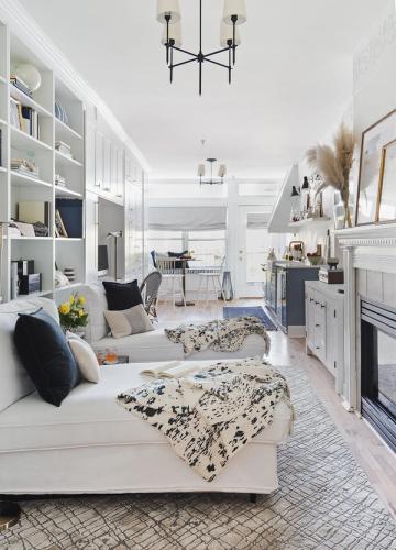 Bright modern living room with white built-in shelving, cream sectional, and patterned throw blankets in a sophisticated neutral palette