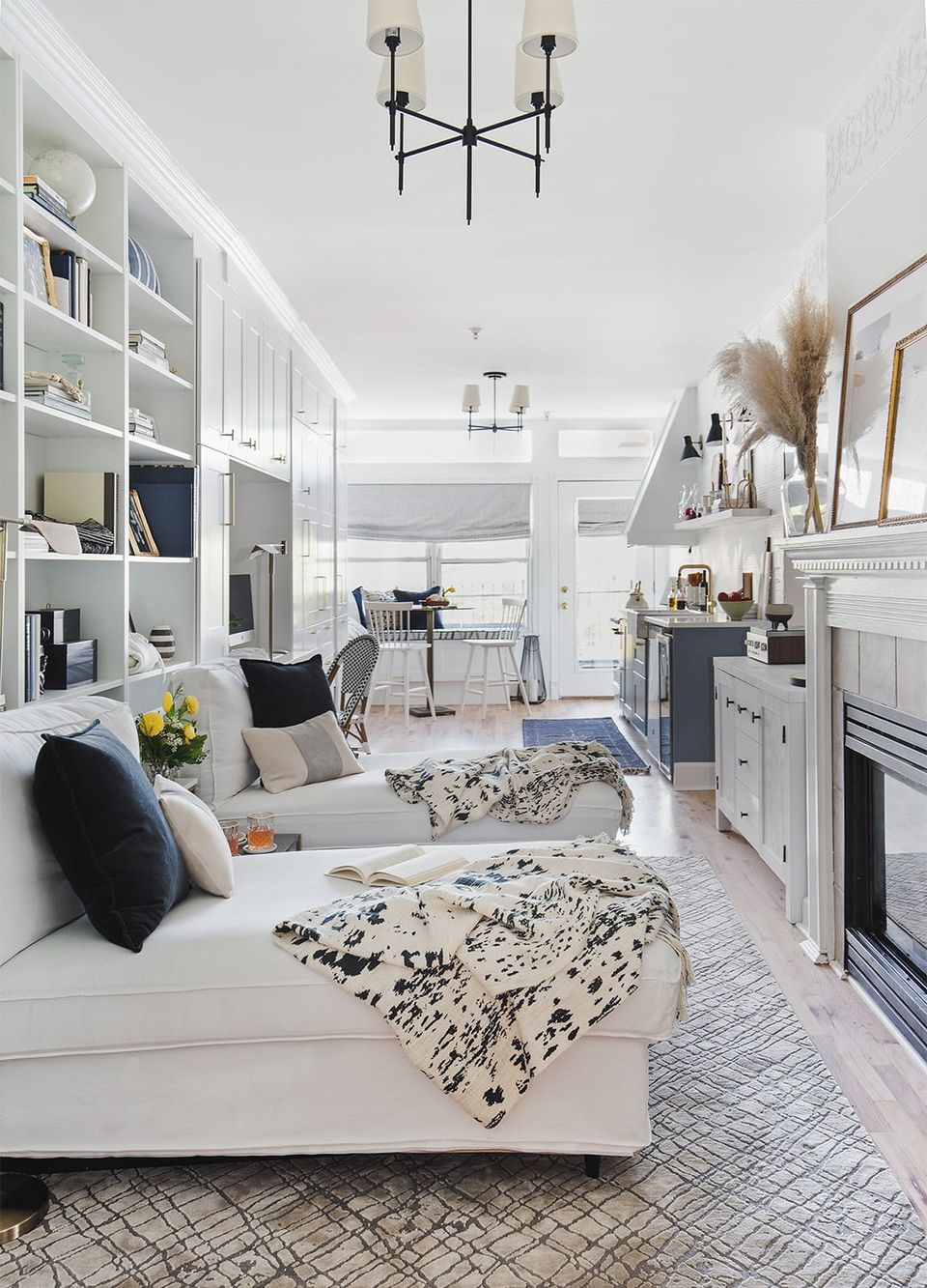 Bright modern living room with white built-in shelving, cream sectional, and patterned throw blankets in a sophisticated neutral palette