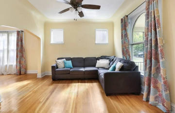 Bright, airy living room with warm yellow walls, dark leather sectional, and patterned curtains creating a welcoming, transitional aesthetic