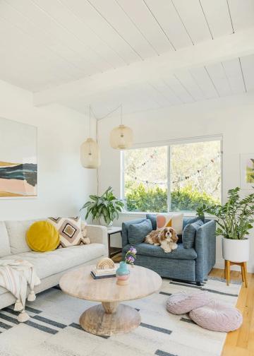 Bright, airy modern living room with round wood table, blue-grey sofa, and playful accents