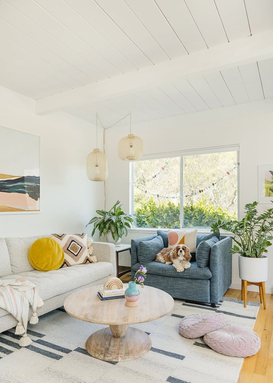Bright, airy modern living room with round wood table, blue-grey sofa, and playful accents