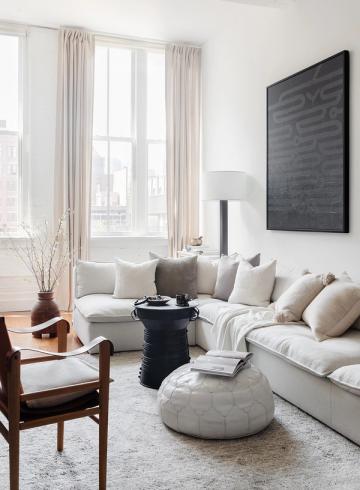 Modern minimalist lounge with cream sectional, floor-to-ceiling windows, and monochromatic black accent wall.