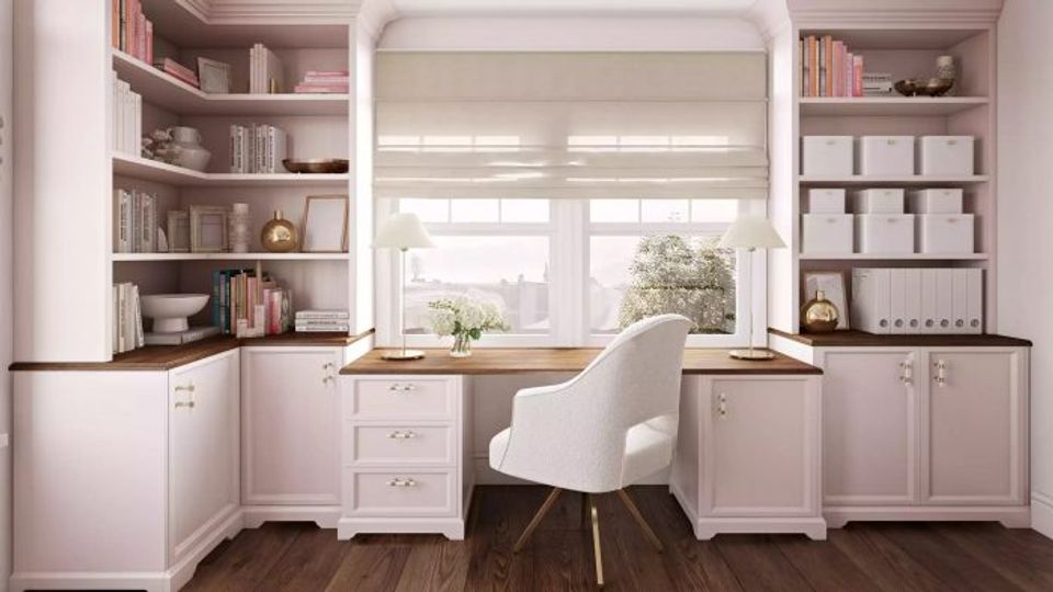 Soft pink built-in workspace with abundant shelving, cream chair, and warm wood accents in a bright, organized feminine office.