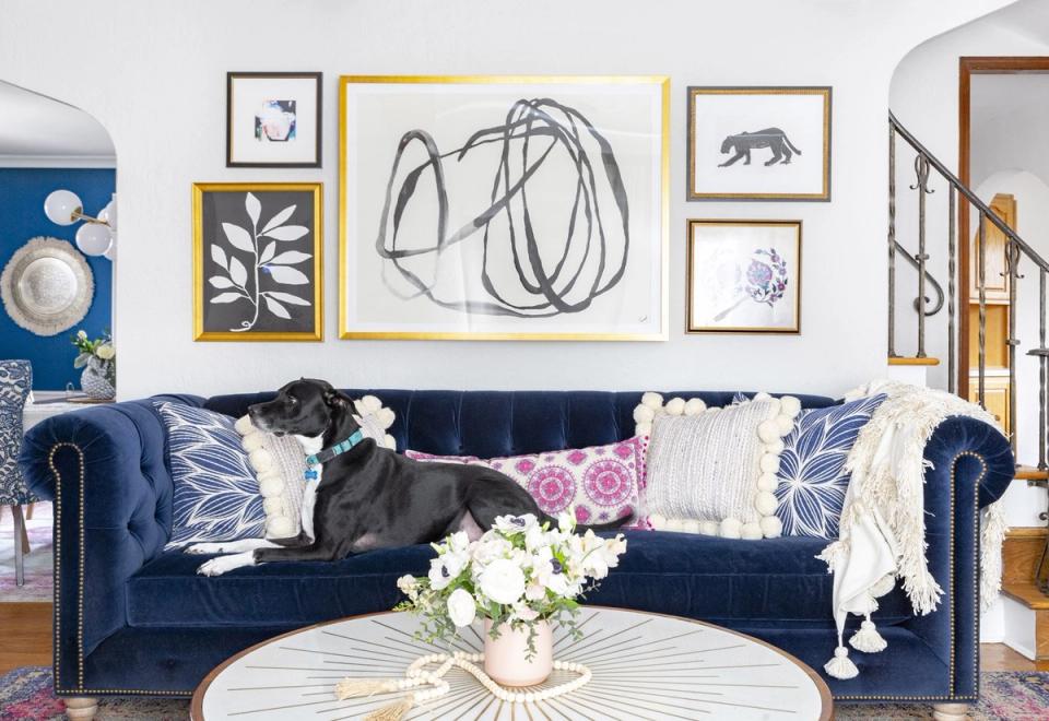 Eclectic gallery wall with mixed-frame artwork in navy, gold, and natural wood tones above a navy velvet sofa