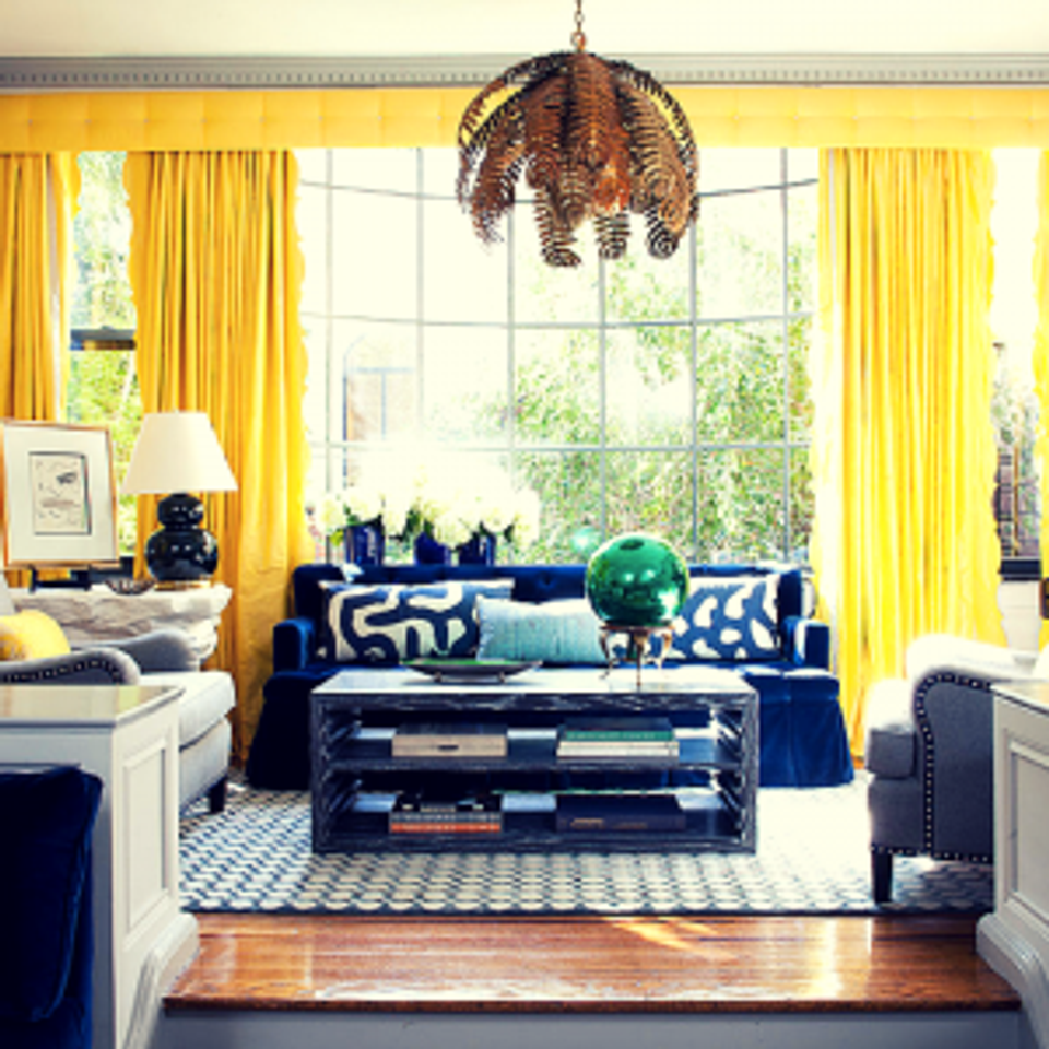 Sophisticated salon: golden drapery, navy sofa, emerald accent chair, and woven pendant light