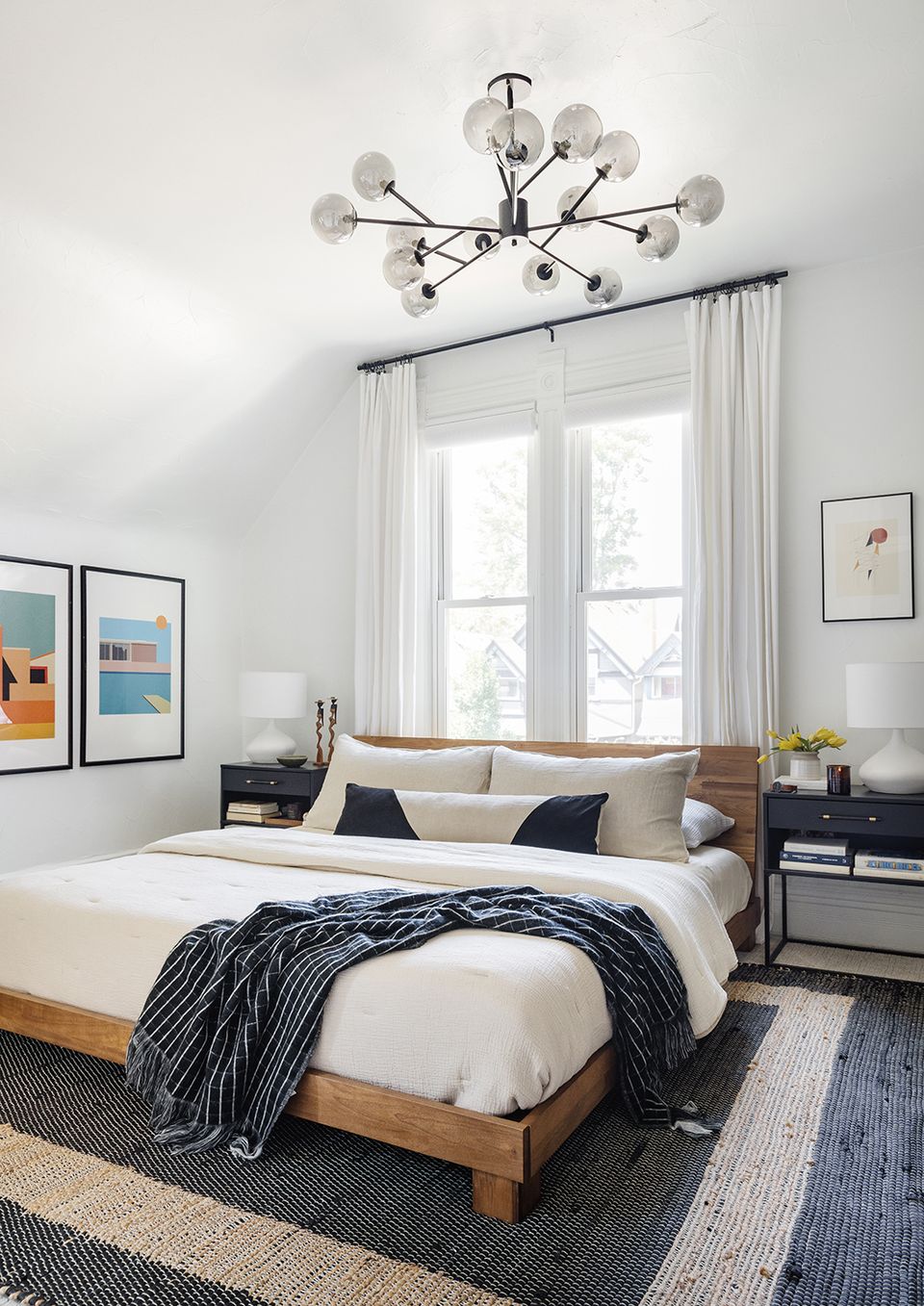 Serene mid-century bedroom featuring sputnik chandelier, natural wood platform bed, navy accents, and soft color palette.