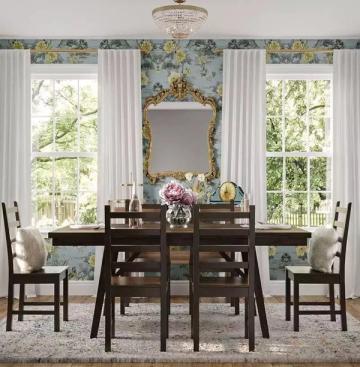 Transitional dining room pairing classical ornate gold mirror with modern dark wood table and soft botanical wallpaper backdrop