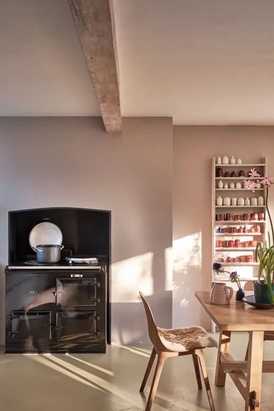 Rustic kitchen with soft mauve walls, black vintage stove, natural wood accents, and open shelving in warm, inviting Scandinavian style.