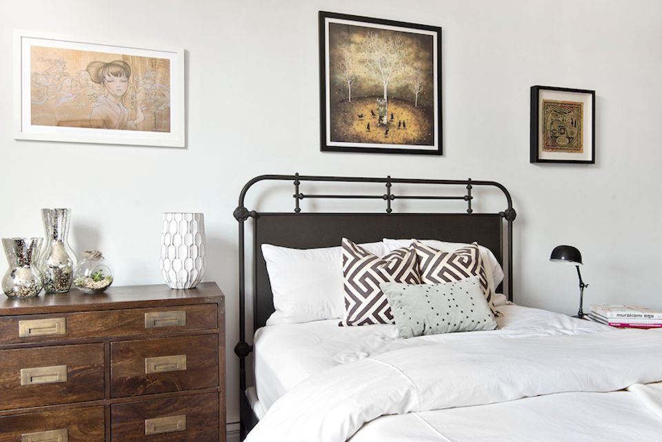 Scandinavian-industrial bedroom combining black metal headboard with mid-century wood dresser and gallery wall art.