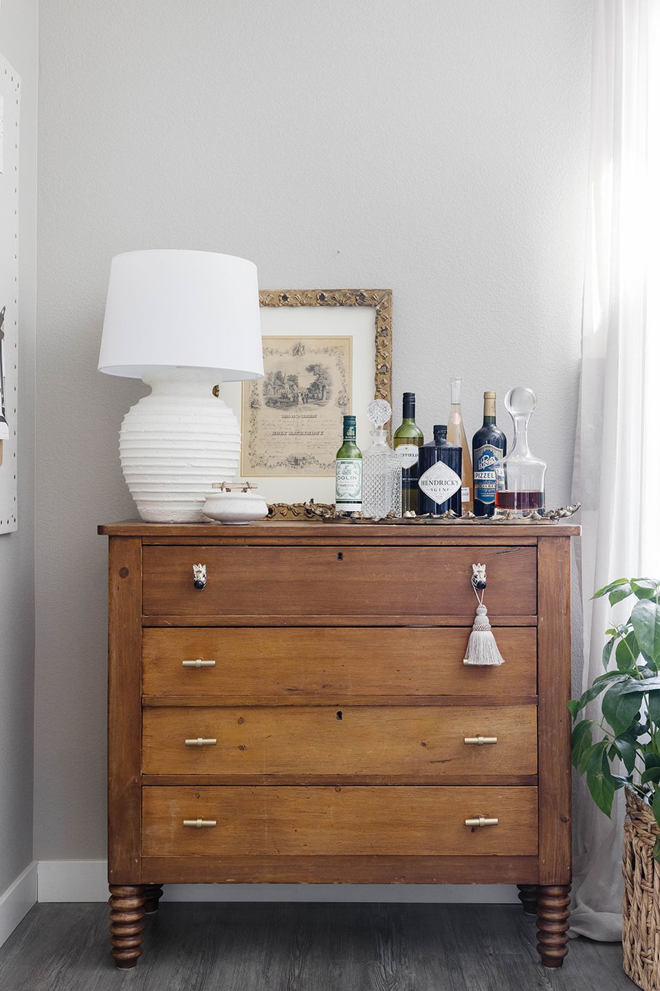 Vintage-styled dresser vignette with warm wood tones, white ceramic lamp, and curated accessories