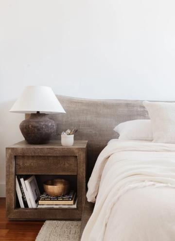 Warm minimalist bedroom with textured wood nightstand, white lamp, and neutral linens.