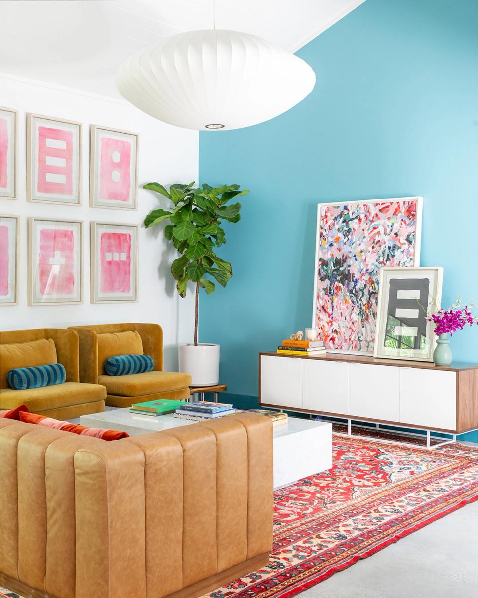 Bold contemporary living room: vibrant turquoise walls, golden mustard sofa, pink gallery grid, and eclectic patterned textiles create playful, energetic mood
